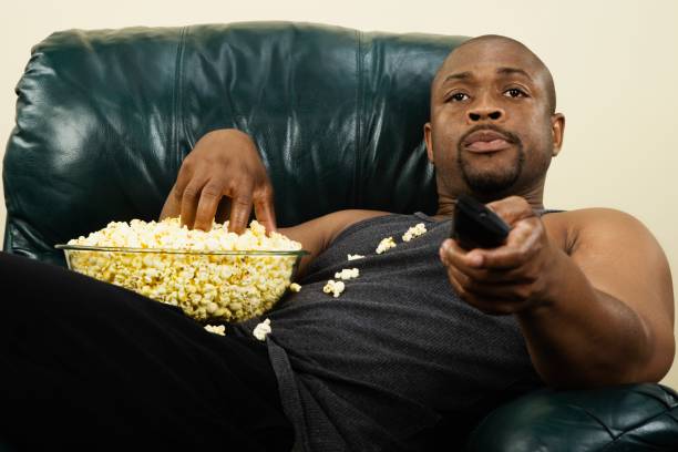 African man sitting in armchair with popcorn and remote control picture id73230368