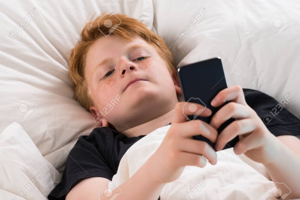 61416971 boy lying on bed holding mobile phone