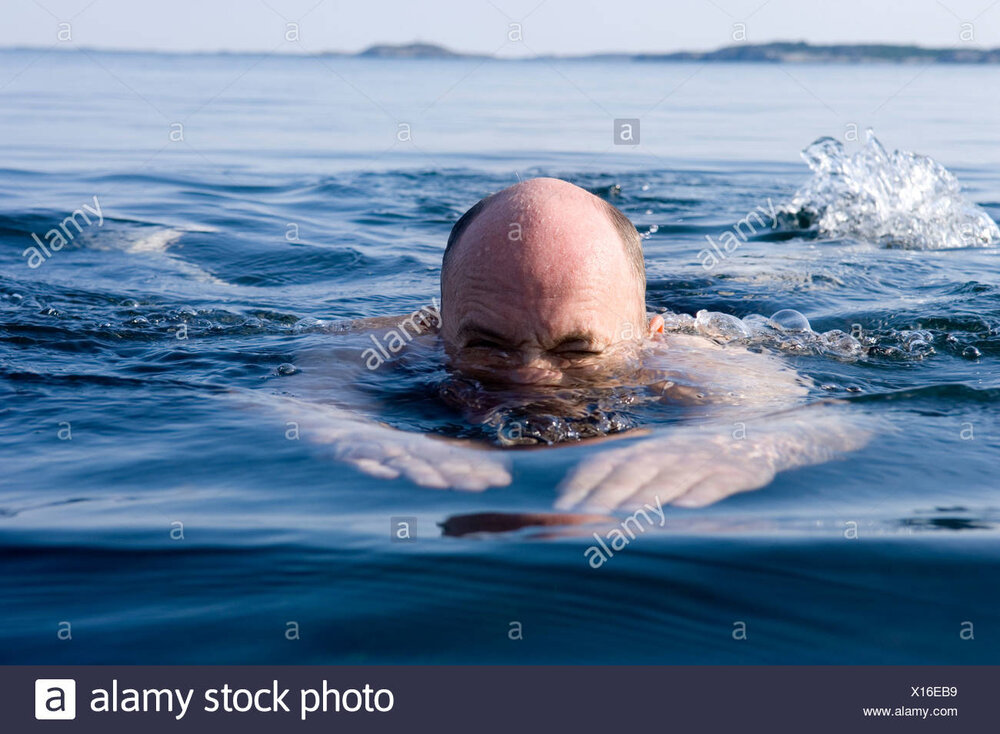 Headshot of a bald man swimming in blue water X16EB9
