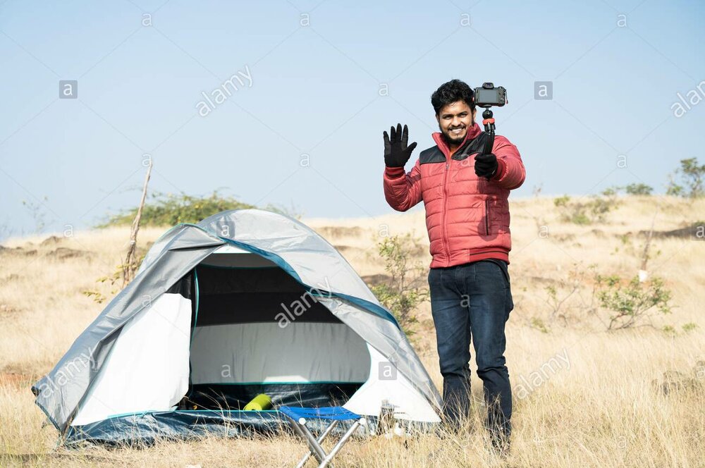 Wide angle shot of young traveller busy talking with camera on top of mountain in front of cam