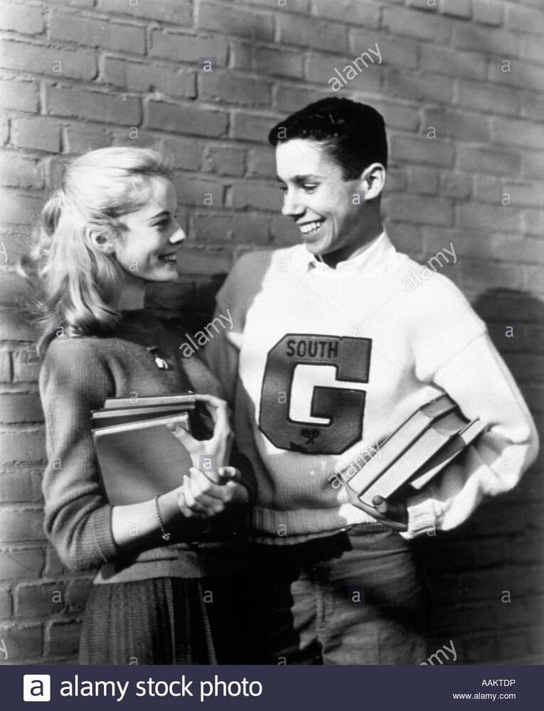 1950s teenage couple holding books and smiling leaning against wall AAKTDP