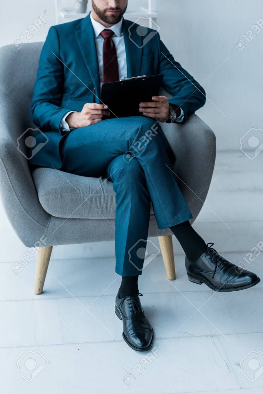 128157413 cropped view of bearded man sitting in crossed legs and holding clipboard