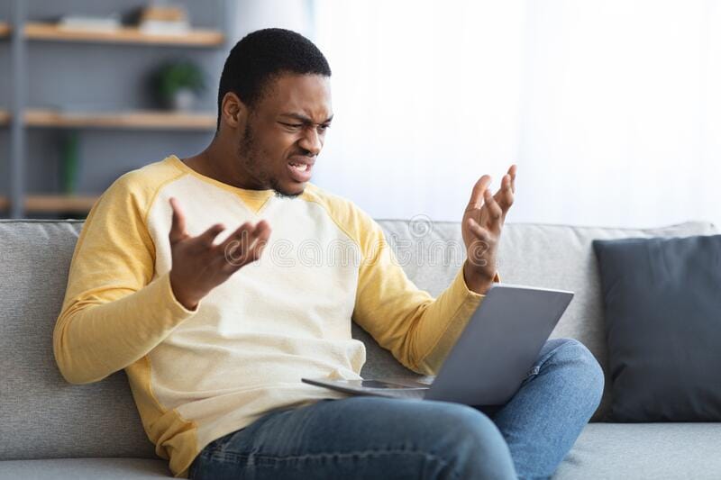 Angry young black man looking laptop screen gesturing losing gambling gaming online sitting co