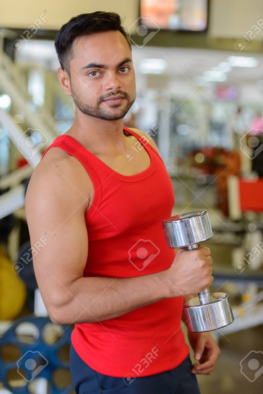 146008264 young handsome bearded indian man lifting weights at the gym
