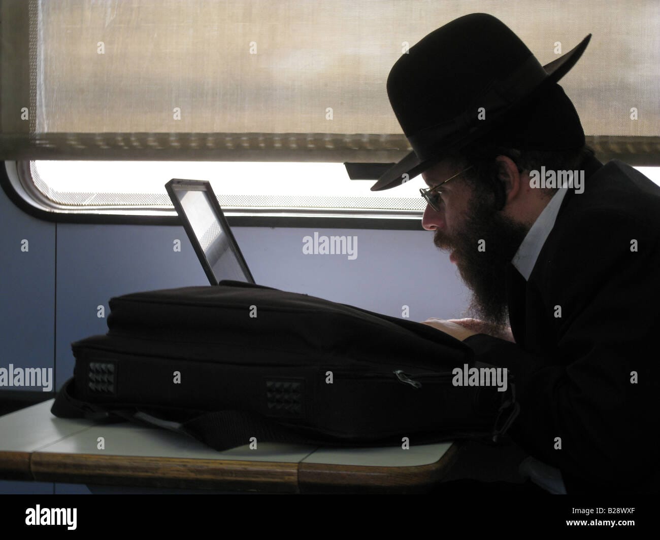 Ultra orthodox jewish passenger with laptop computer seated in train B28WXF