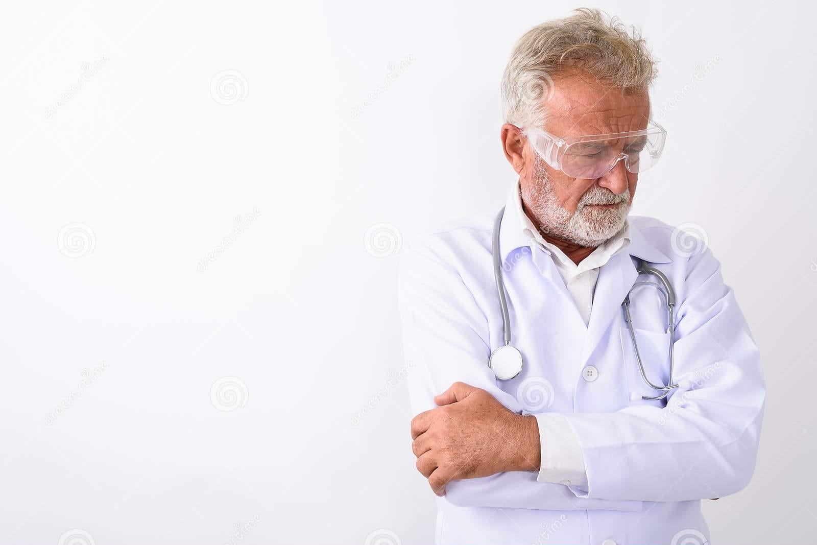 Studio shot sad senior bearded man doctor thinking wearing protective glasses arms crossed aga