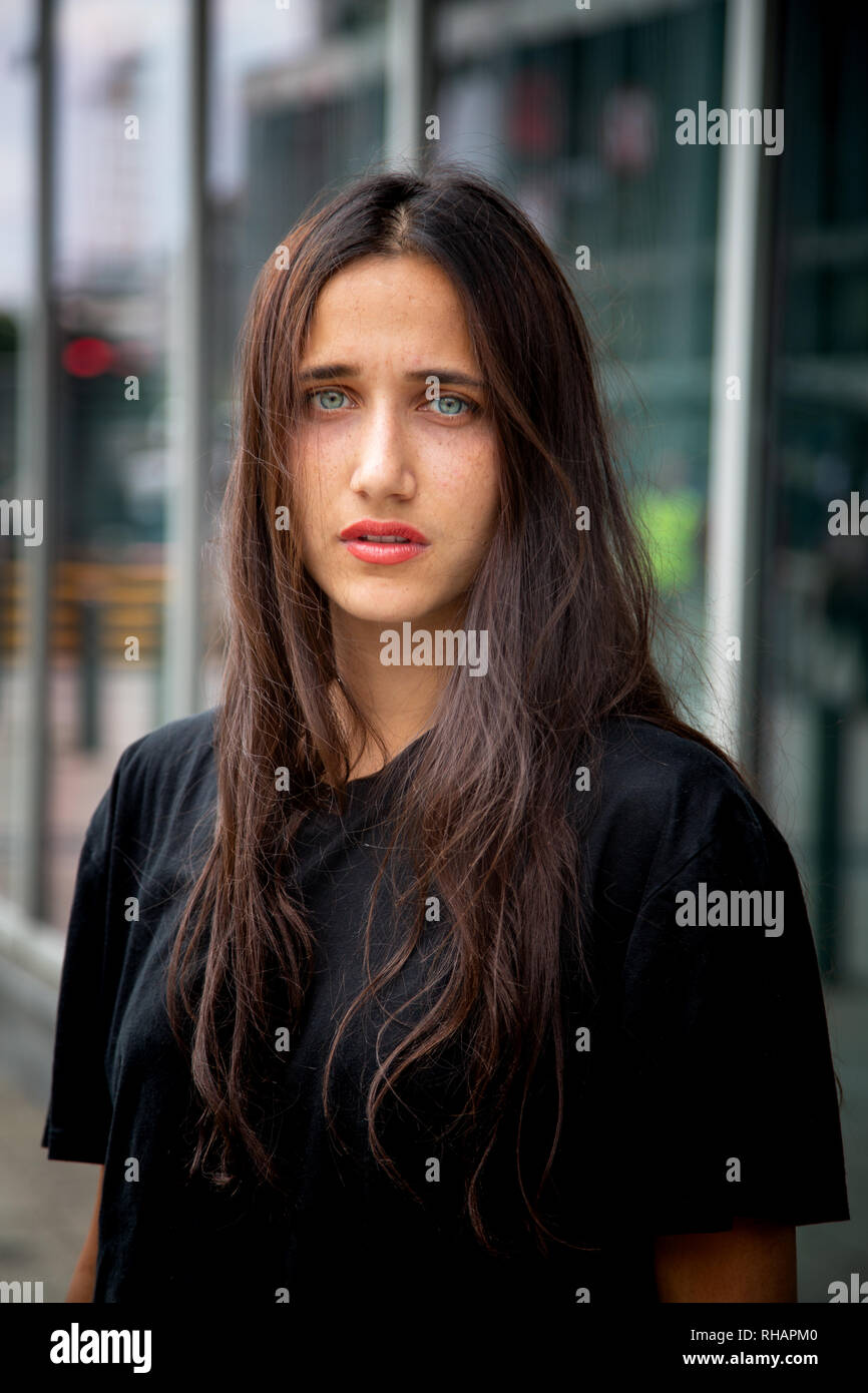 Beautiful olive skinned young woman with light colored eyes standing outdoors in urban setting