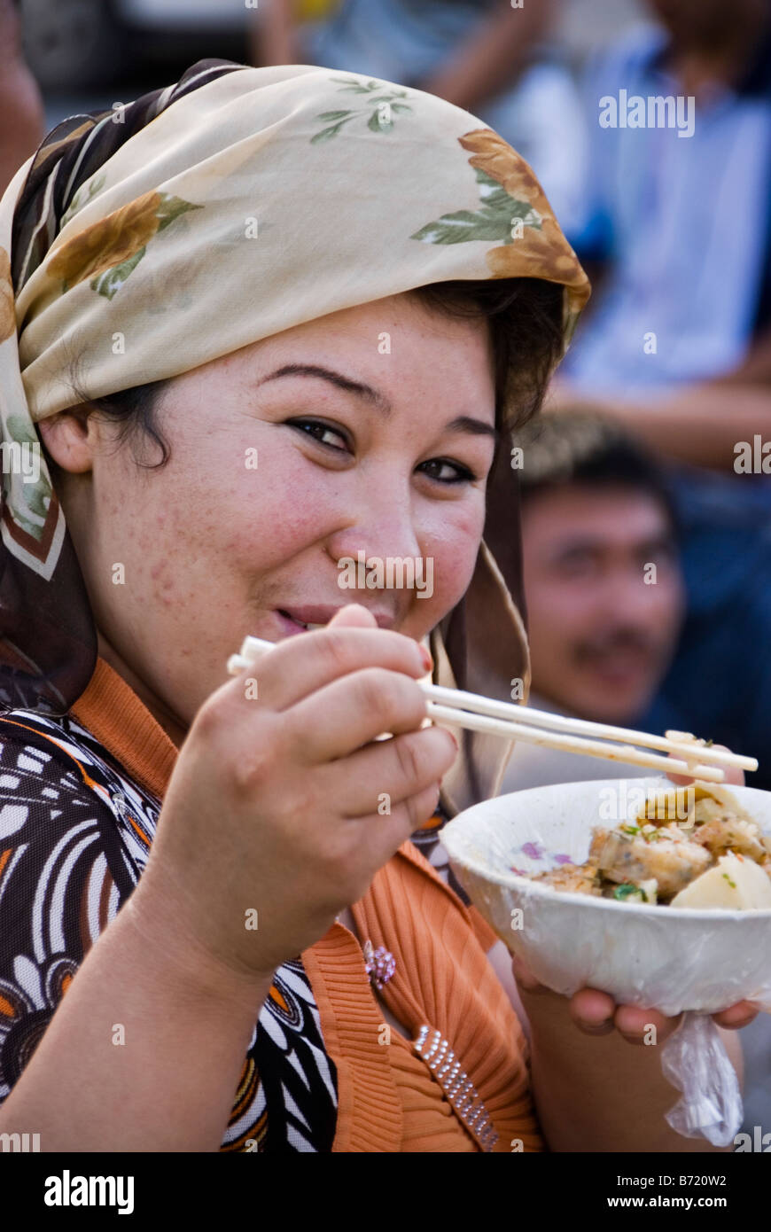 Woman eating with chopsticks in the street kashgar xinjiang china B720W2