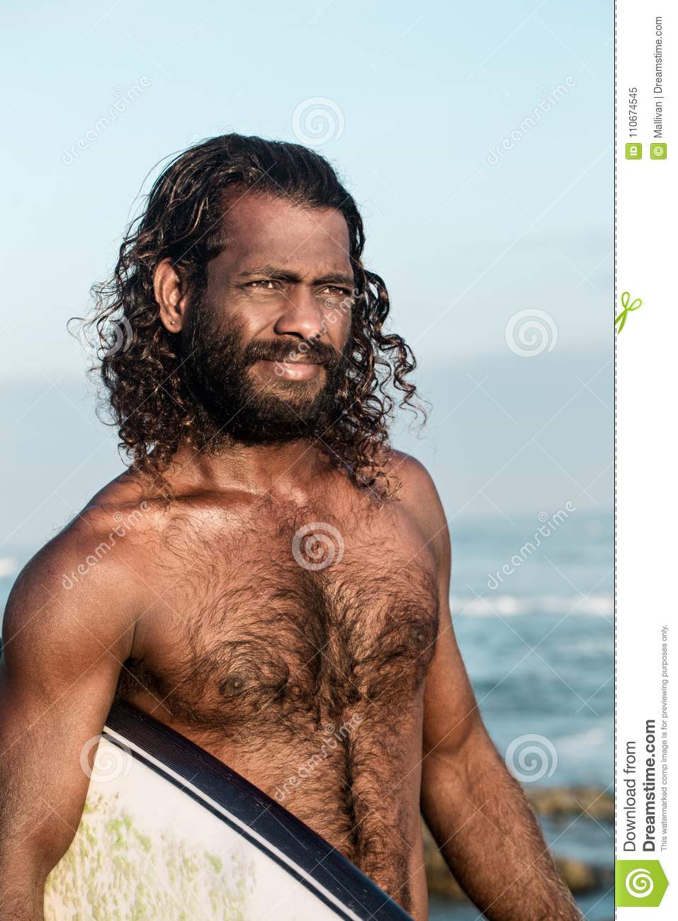 Surfer holding surfboard indian ocean shore portrait long haired man 110674545