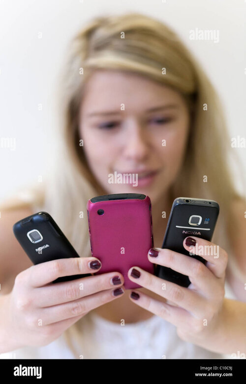 blond-teenage-girl-holding-and-looking-at-3-mobile-phones-C10C9J.jpg