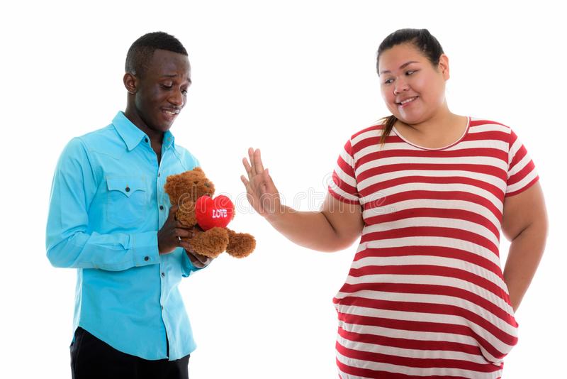 Happy young black african man giving teddy bear heart love sign to fat asian woman smiling sho