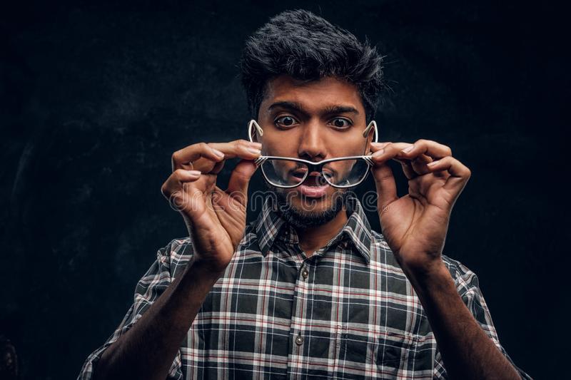Surprised indian guy lowers his glasses realizes now can see studio photo against dark texture