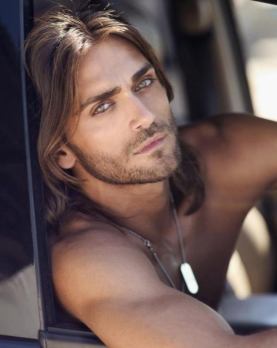 A picture of a green eyed male with long wavy hair ready to drive off in his car