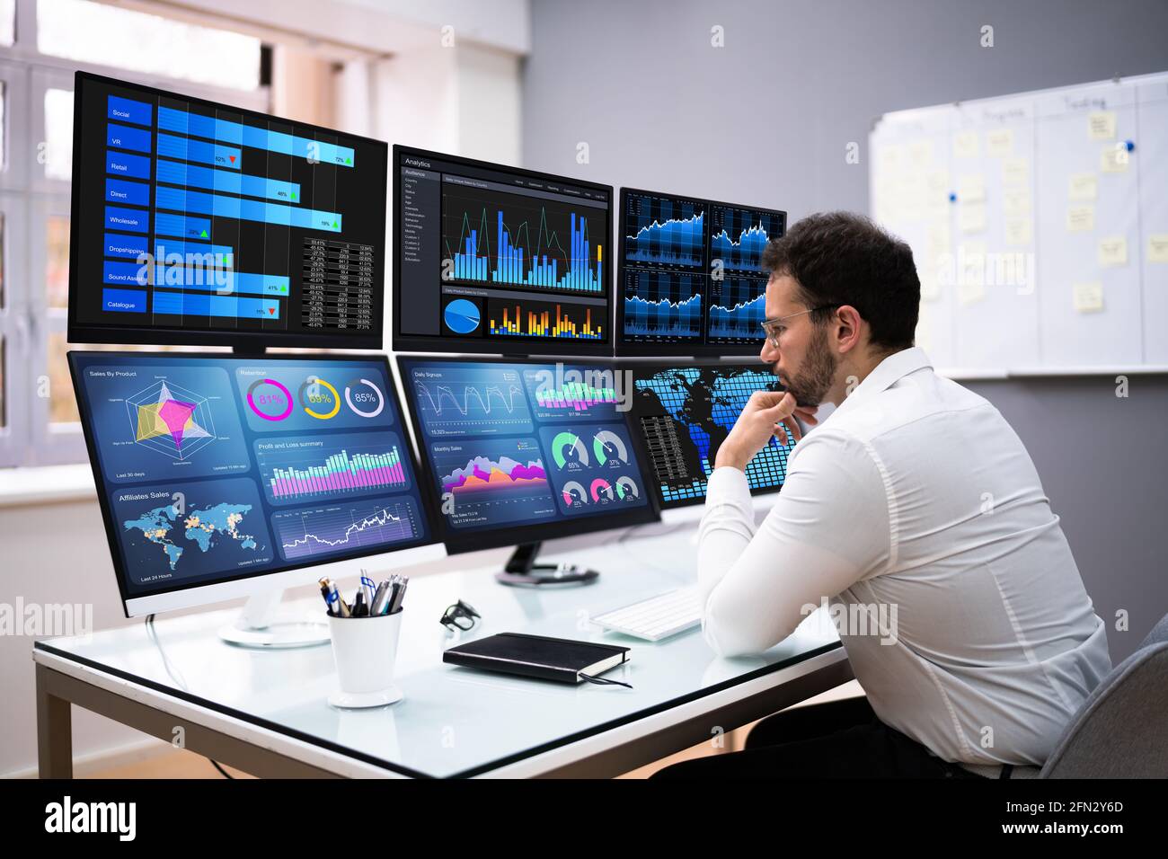 Stock trader man using multiple computer monitors 2FN2Y6D