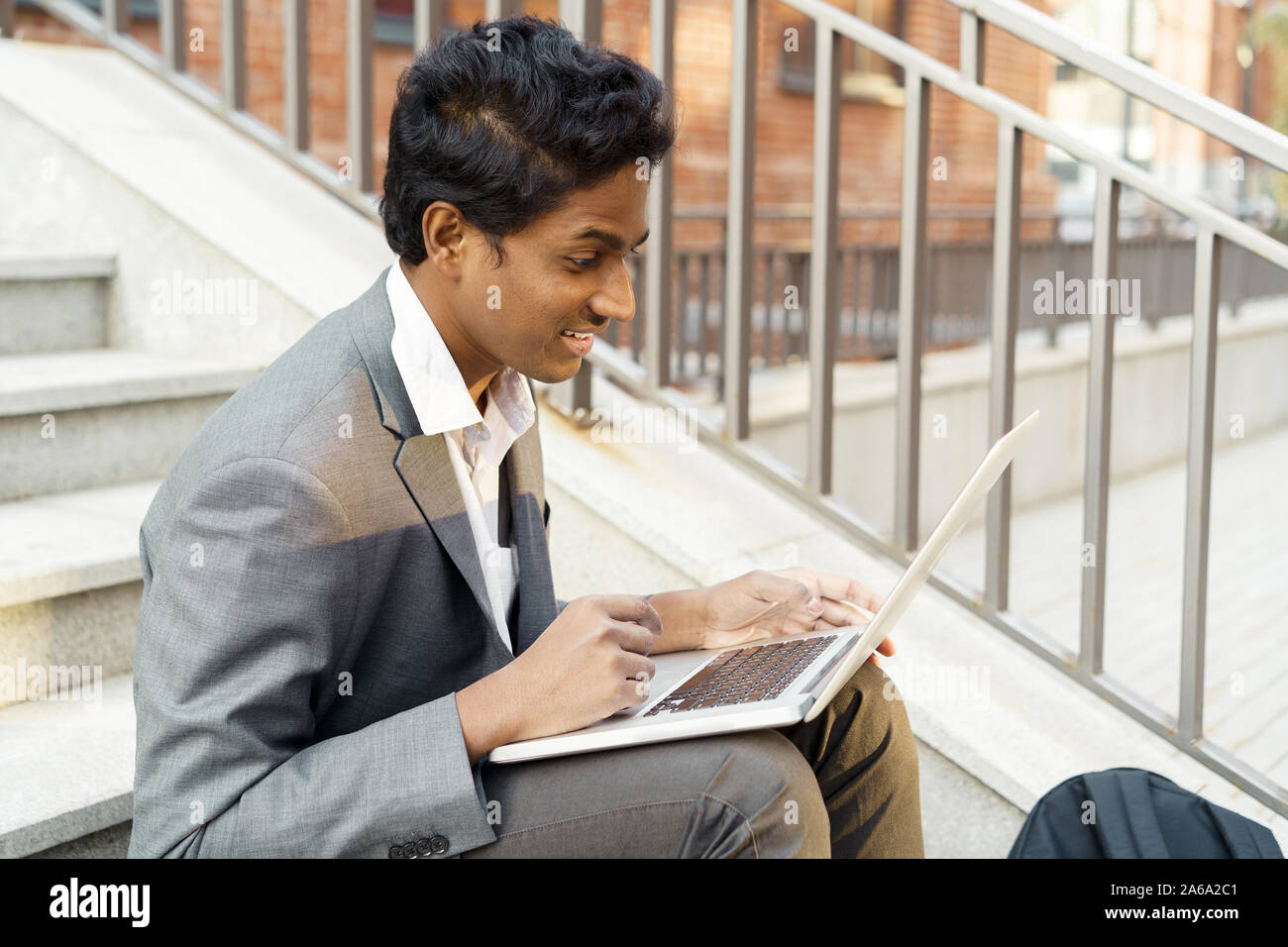 Young handsome indian man is sitting with a laptop smiling and typing 2A6A2C1