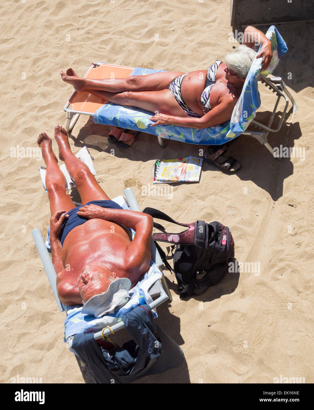 Elderly couple with deep tans sunbathing on beach in spain EKY6NE