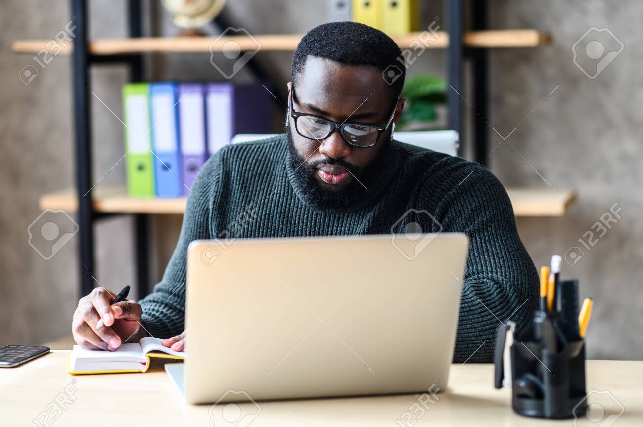 150009549 focused black guy sits at the desk with a laptop in office space an african american