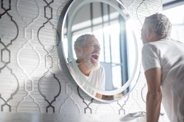 Morning mirror gray haired man with open mouth standing front mirror looking his reflection 25 Morning mirror gray haired man with open mouth standing front mirror looking his reflection 25
