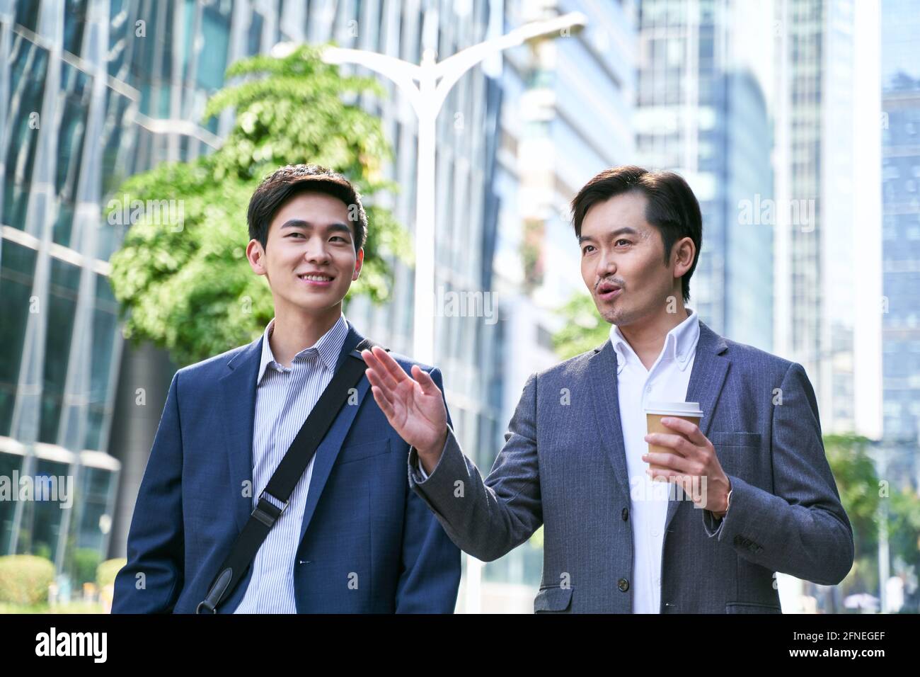 Two asian business people walking talking on street in modern city 2FNEGEF