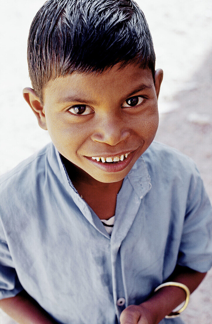 70188494 Young Indian boy with a big smile and wet hair wearing a blue shirt looking up