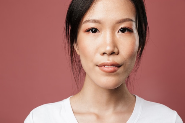 Portrait beautiful asian woman dressed basic wear smiling with lovely glance isolated red wall