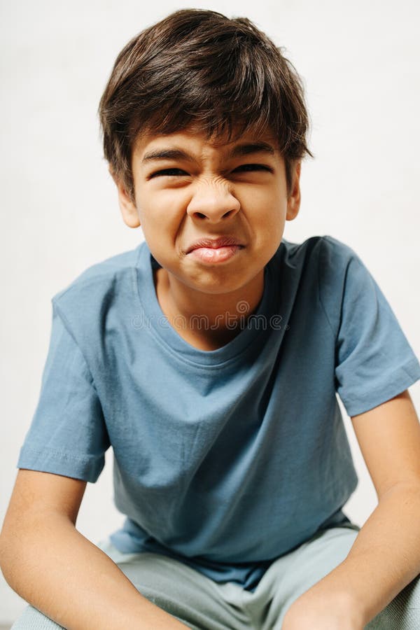 Grimacing indian boy sitting wrinkled tense face over white background wears simple cotton shi