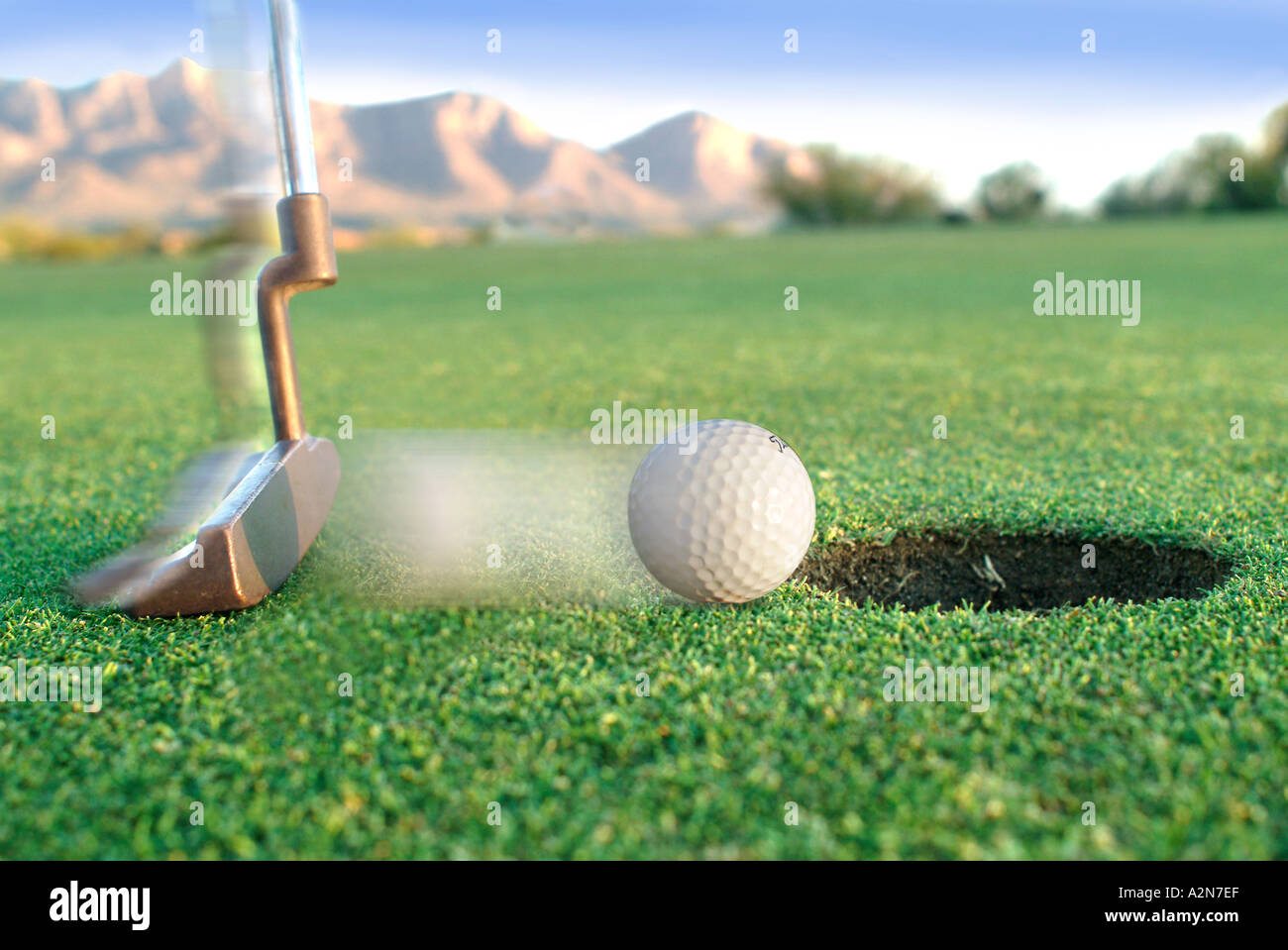 Blurred golf ball being putted into hole on putting green A2N7EF
