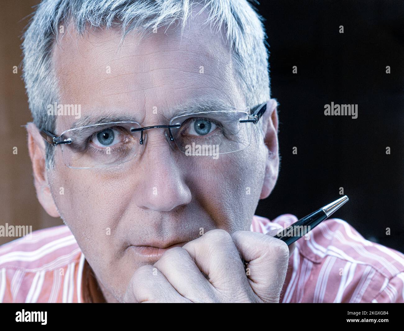 Businessman man male 50s face mature wearing glasses close up with hand on chin holding a pen 