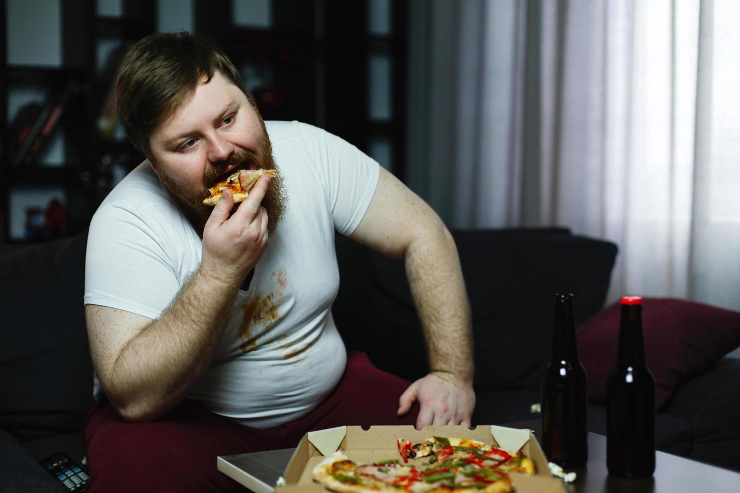 Ugly fat man eats pizza sitting on the sofa free photo