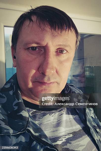 A man with a beard and a mustache is standing in front of a window