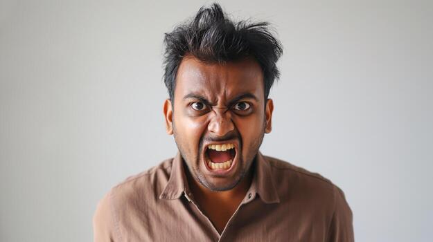 Angry young man with wild hair yelling in brown shirt posing for studio portrait with white ba