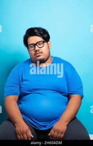 Porrait of a fat man wearing eyeglasses sitting with a dull tired expression on face 2h604dm