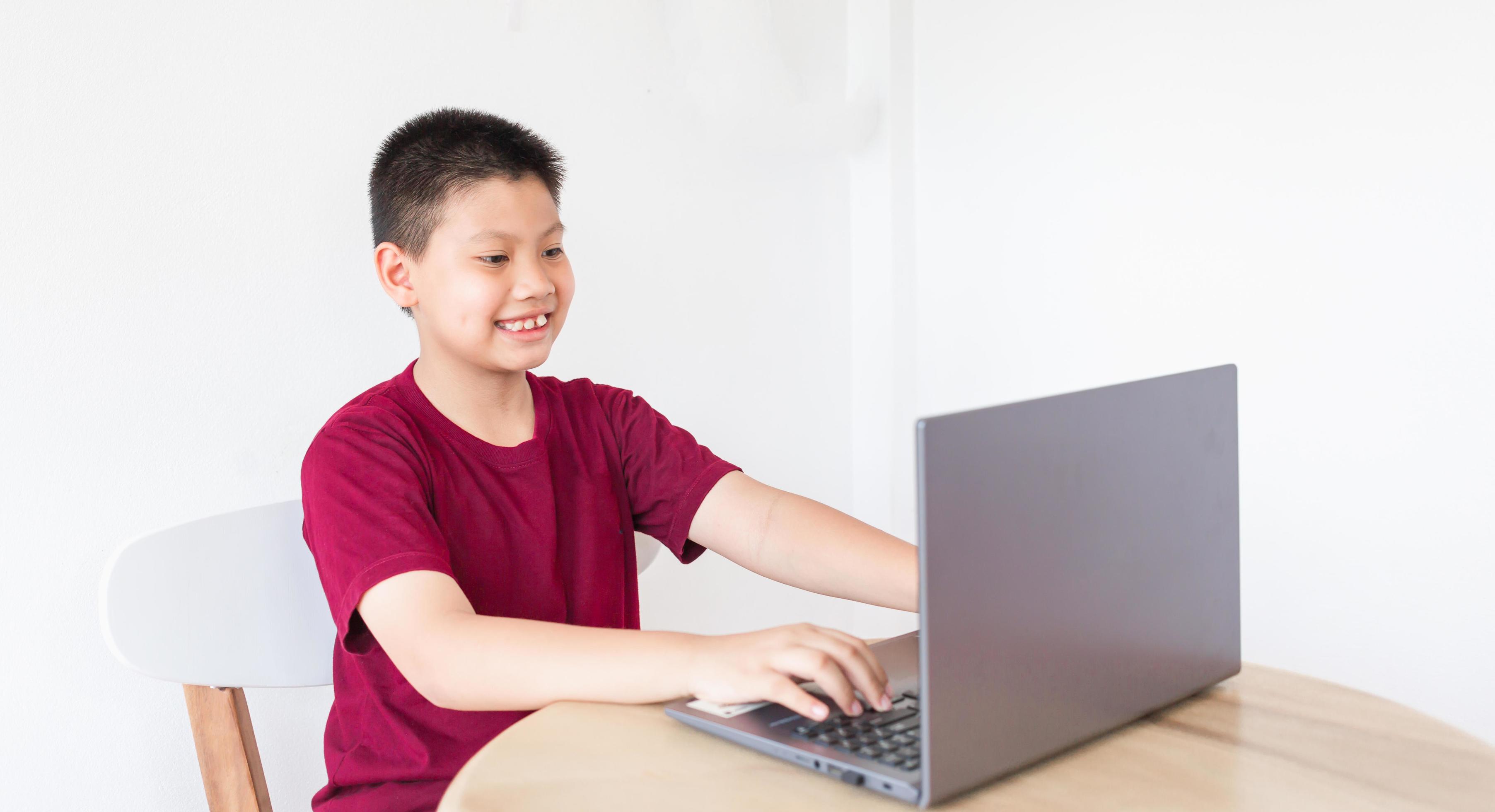 Asian boy studying online on computer laptop with smiling and happy face at home online educat