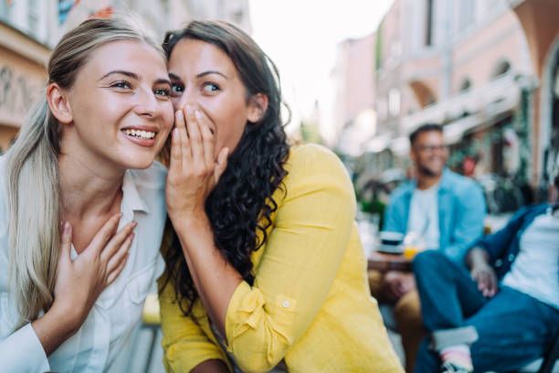 Two female young friends sitting in city cafe and gossiping