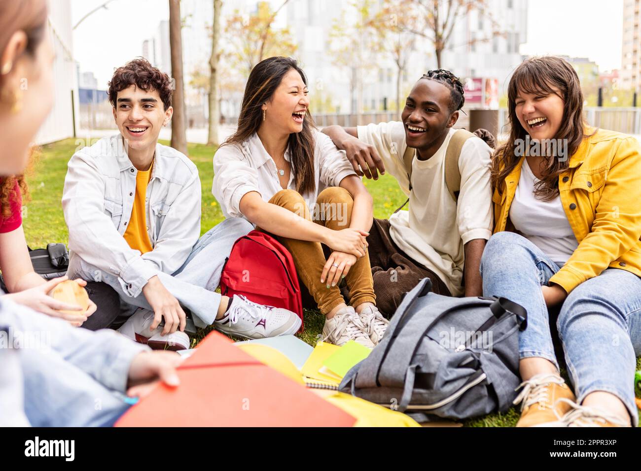 Young group of multiracial students sitting on the grass at university campus 2PPR3XP